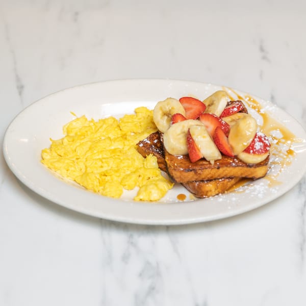 Scrambled eggs and French toast topped with strawberries, bananas, powdered sugar, and syrup.