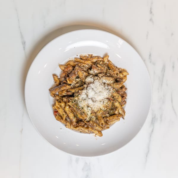 Overhead view of penne pasta with sauce, meat, vegetables, and grated cheese on a white plate.