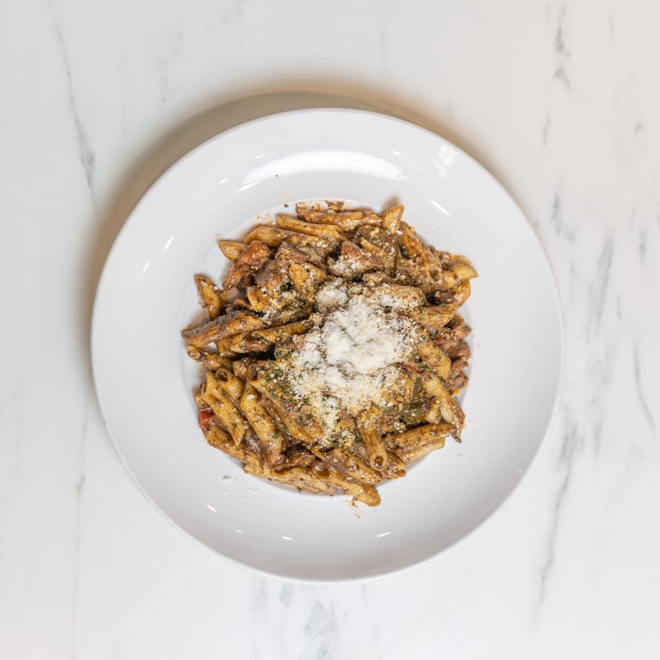 Overhead view of penne pasta with sauce, meat, vegetables, and grated cheese on a white plate.