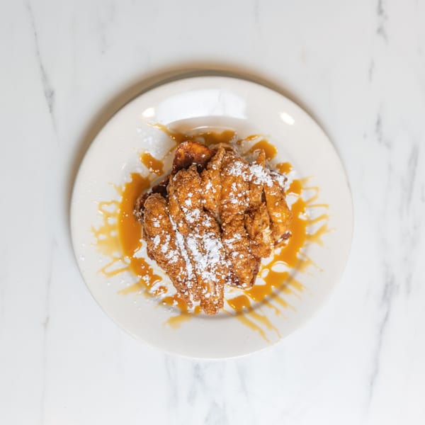 Golden fried chicken and waffles drizzled with caramel sauce and powdered sugar on a white plate.