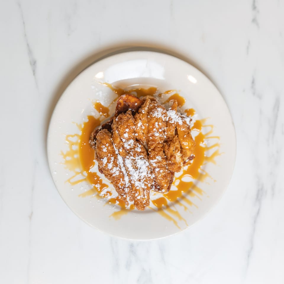 Golden fried chicken and waffles drizzled with caramel sauce and powdered sugar on a white plate.