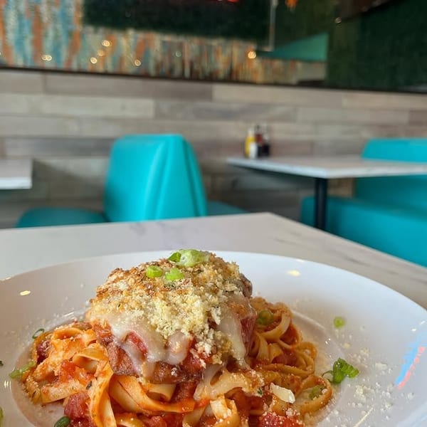 Plate of pasta with meat, melted cheese, and breadcrumbs in Addiction Bistro with turquoise booths.