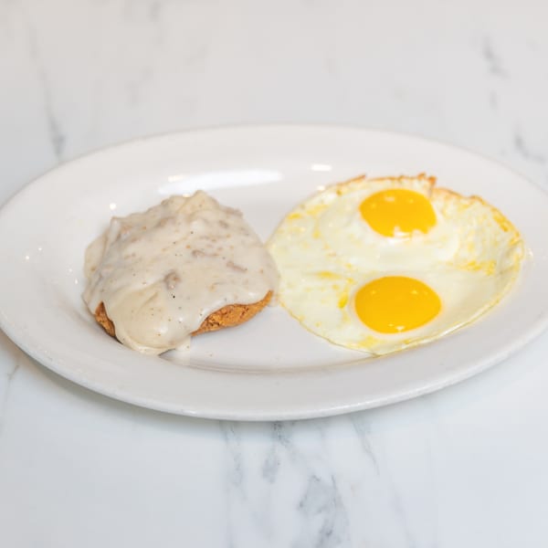 A white plate with a biscuit covered in gravy and two fried eggs with bright yellow yolks.