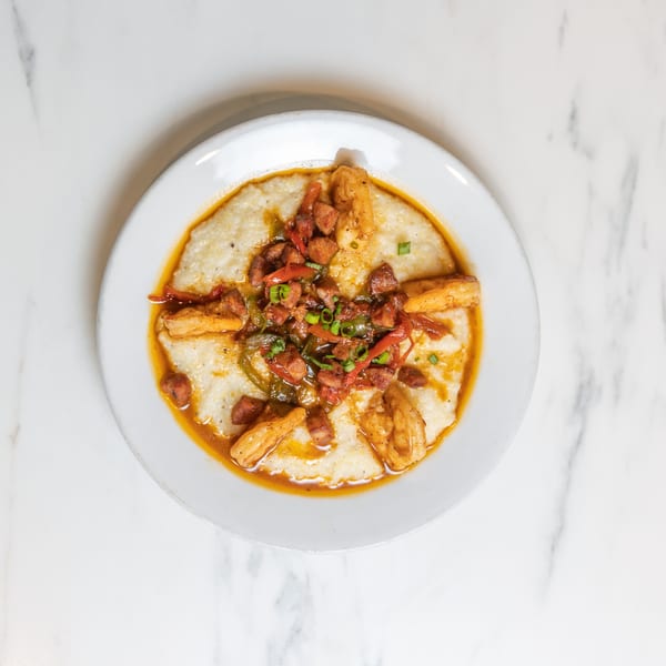 Shrimp and grits with sausage, peppers, and green onions in a white bowl on a marble surface.