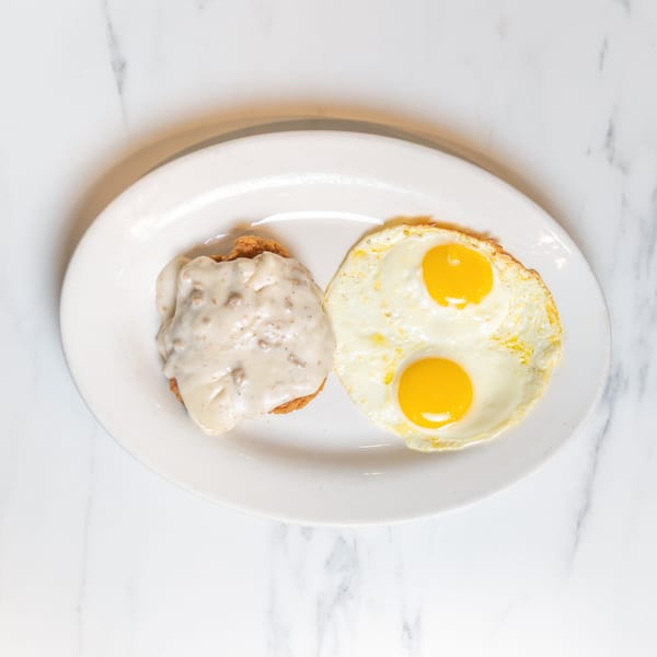 Chicken fried steak with gravy and two sunny-side-up eggs on a white plate.