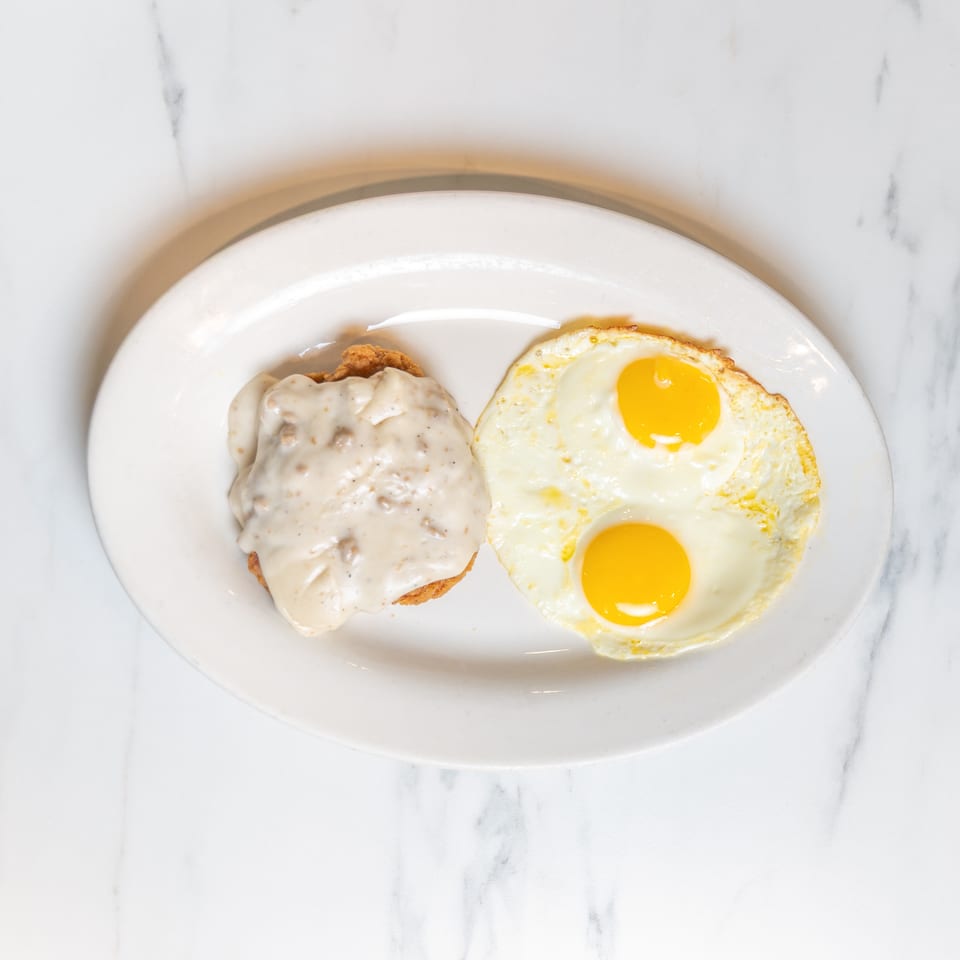 Chicken fried steak with gravy and two sunny-side-up eggs on a white plate.