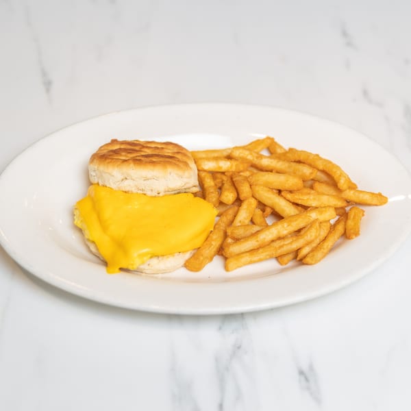 A biscuit with melted cheese and a side of french fries on a white plate.