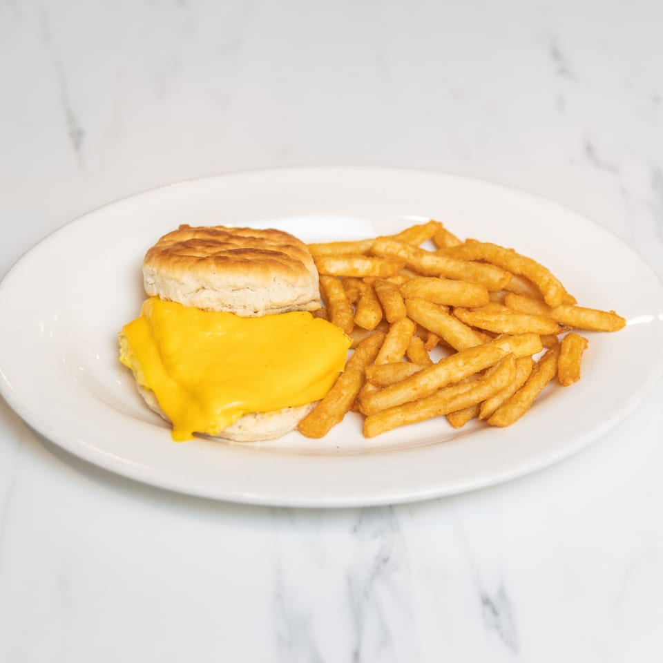 A biscuit with melted cheese and a side of french fries on a white plate.