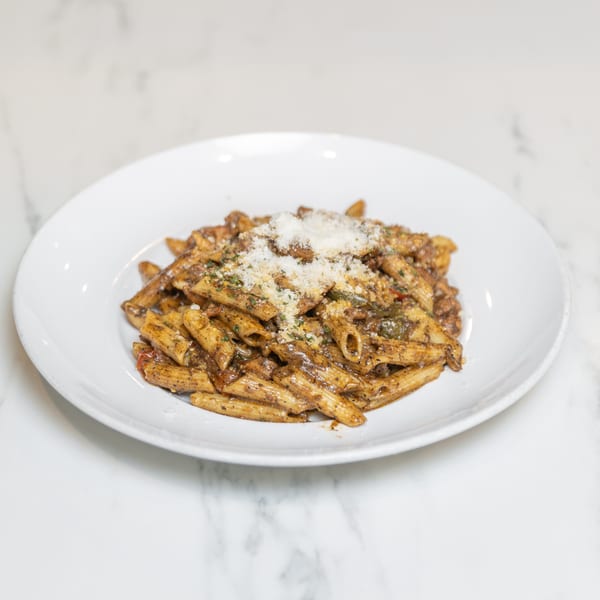 A white plate filled with penne pasta in a rich brown sauce, topped with grated cheese and herbs.