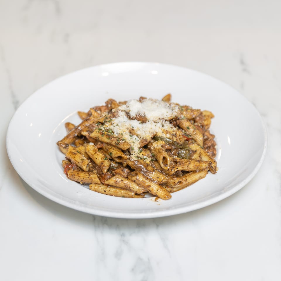 A white plate filled with penne pasta in a rich brown sauce, topped with grated cheese and herbs.