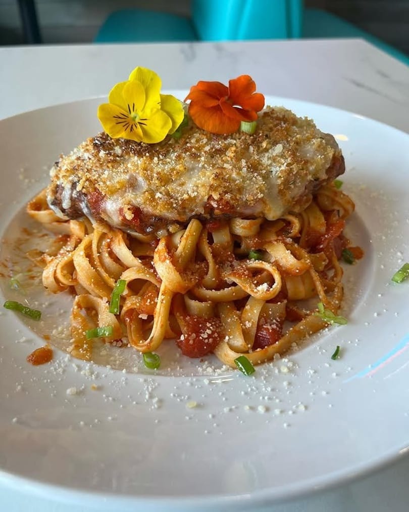 Chicken parmesan over fettuccine pasta with red sauce, garnished with edible flowers and chives.