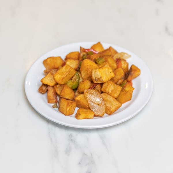 A white plate filled with golden-brown home fries, mixed with green and red bell peppers and onions.