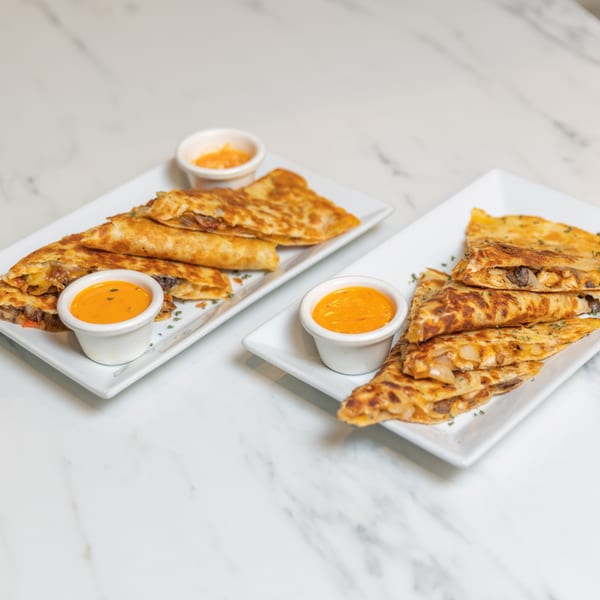 Two plates of golden-brown quesadillas, each with a side of orange dipping sauce, on a marble surface.