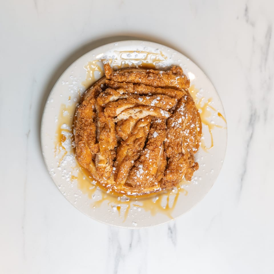 Crispy fried chicken strips on a waffle, drizzled with syrup and powdered sugar on a white plate.
