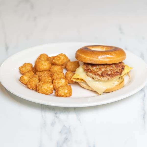 Breakfast bagel sandwich with sausage, egg, and cheese, served with a side of tater tots.