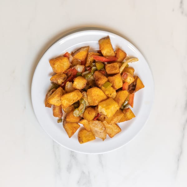 A white plate filled with golden-brown home fries, mixed with sautéed onions, red and green bell peppers.