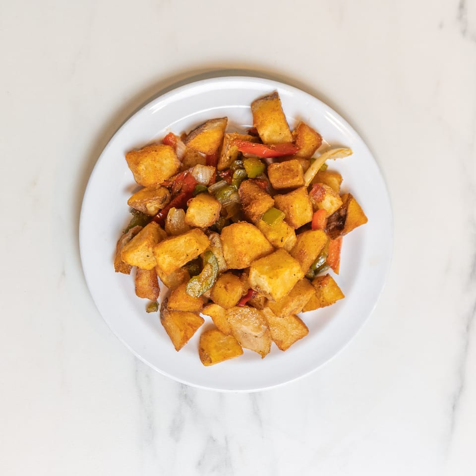 A white plate filled with golden-brown home fries, mixed with sautéed onions, red and green bell peppers.