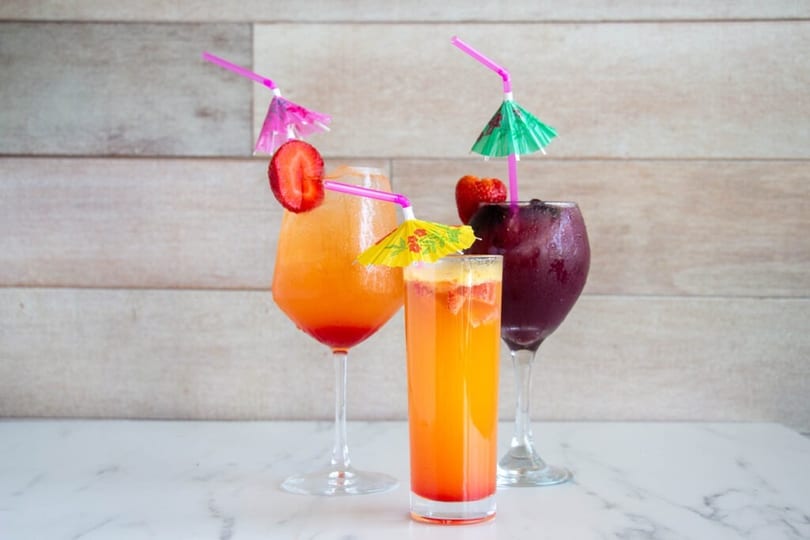 A trio of colorful, fruity cocktails with decorative umbrellas and strawberry garnishes.