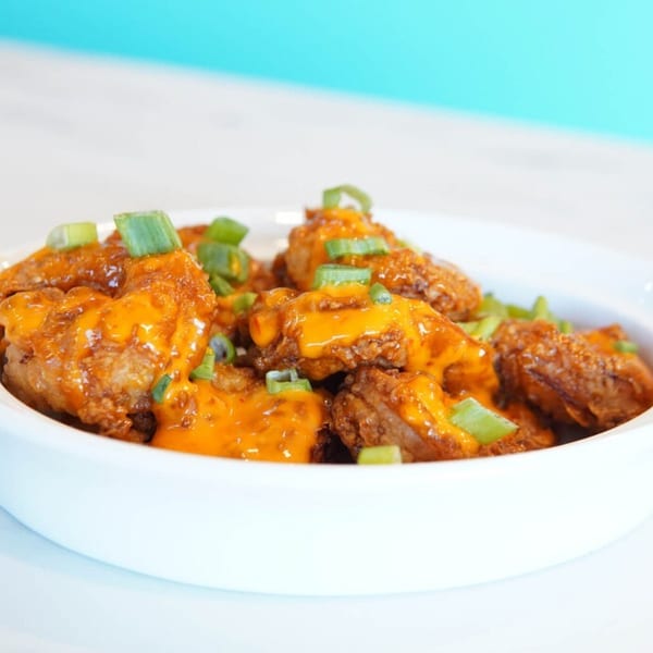 Crispy fried chicken bites drizzled with orange sauce and garnished with green onions.