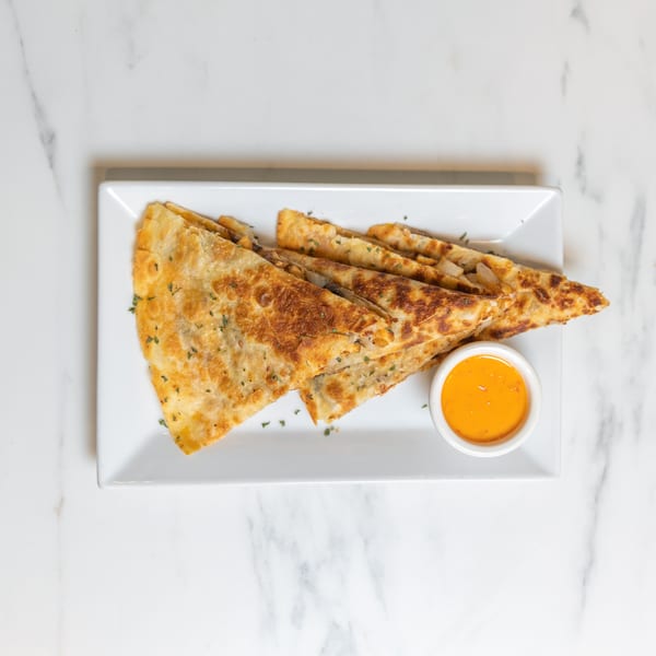 Golden-brown quesadilla triangles with herbs and a side of orange dipping sauce on a white plate.