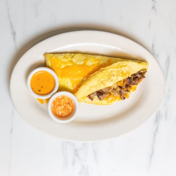 A cheese and meat omelet with two small bowls of orange sauce on a white plate.