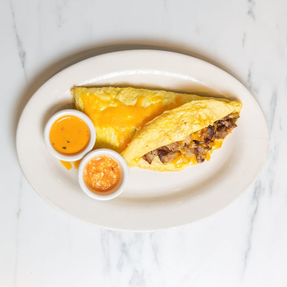 A cheese and meat omelet with two small bowls of orange sauce on a white plate.