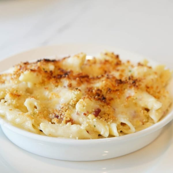 Baked penne mac and cheese with a golden breadcrumb crust in a white serving bowl.