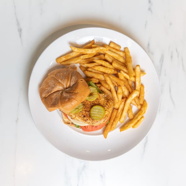 Grilled chicken sandwich with pickles, tomato, onion, lettuce, and a side of french fries.