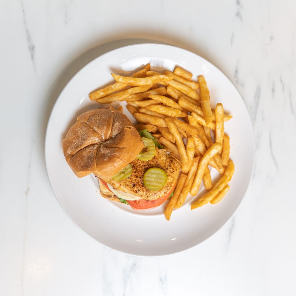 Grilled chicken sandwich with pickles, tomato, onion, lettuce, and a side of french fries.
