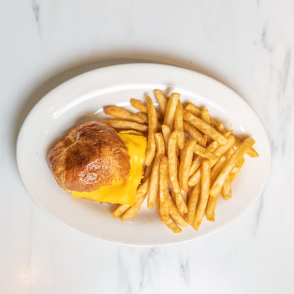 A golden-brown croissant sandwich with melted cheese and a side of crispy french fries on a white plate.